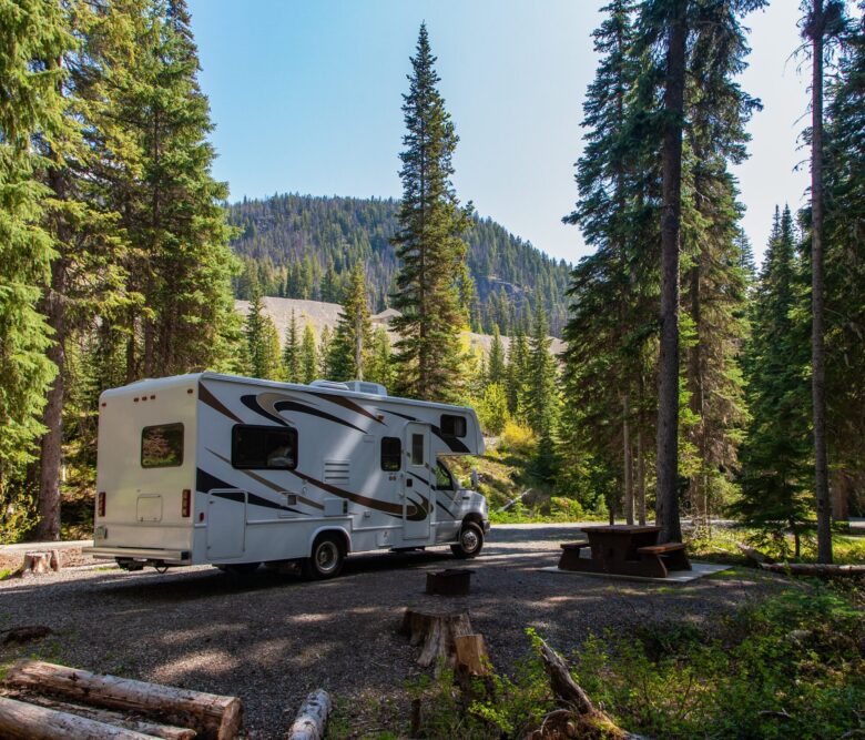 JASPER, CANADA - Jun 03, 2019: Beautiful campsite in the forest on a lovely sunny day. There is an RV and a wooden bench and a mountain in the background.